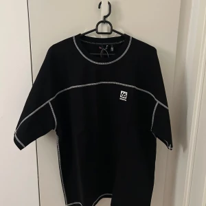 66 North Svart t-shirt med kontrastsömmar XL - Svart t-shirt från 66 North med vita kontrastsömmar och logga på bröstet. Oversized passform och rund halsringning. Perfekt för en clean och modern look.