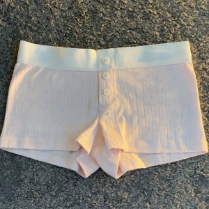 Söta ljusrosa shorts med knappar från Gina Tricot - Säljer ett par gulliga ljusrosa shorts från Gina Tricot med bred vit resår i midjan och tre dekorativa knappar framtill. Shortsen har diskret hålmönster och är supermjuka och bekväma. Inte använt någon gång och ser helt nya ut, skriv privat ifall du har frågor💞💞