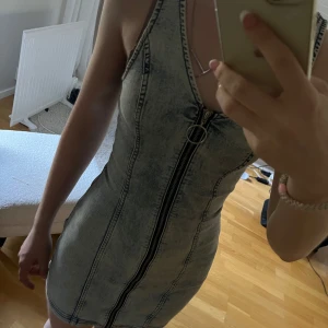 Ljusblå jeansklänning med dragkedja - Säljer en tight, ärmlös ljusblå jeansklänning med markerade sömmar och hel dragkedja framtill. Klänningen har en snygg, figurnära passform och är perfekt för dig som gillar denim. Passar till många olika tillfällen och är superenkel att styla.