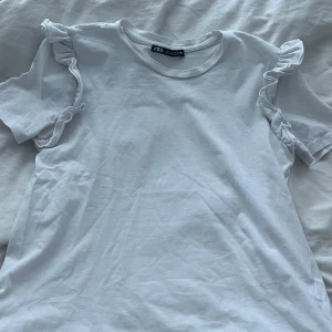 Vit t-shirt från Zara - Säljer en vit t-shirt från Zara med volangdetaljer på axlarna. Hör av er vid frågor, annars är det bara att klicka på köp nu!❤️
