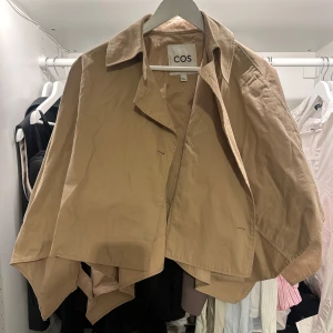 Beige croppad trenchcoat från COS - Kollar intresset på min trench/cape från cos då den inte säljs längre! Den är inte använd mycket så i väldigt bra skick! 🌸☀️