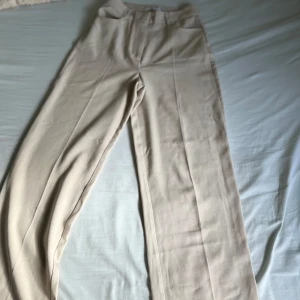 Beiga kostymbyxor från NA-KD - Snygga beiga kostymbyxor från NA-KD med raka ben och hög midja. Byxorna har klassisk passform, bälteshällor och diskreta fickor framtill. Perfekta för en stilren look.