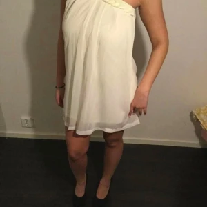 Vit one shoulder klänning - Säljer en söt vit kortklänning med one shoulder-design och draperad detalj upptill. Klänningen har en luftig passform och är perfekt för sommarens tillfällen. Stilren och enkel att matcha med accessoarer.passar 34-38(40)