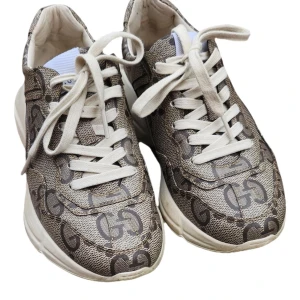 Beige sneakers från Gucci med GG-mönster - Säljer ett par beige sneakers från Gucci med klassiskt GG-mönster över hela skon. Skorna har vita snören, rund tå och tjock vit sula. Perfekta för dig som vill ha en lyxig och trendig look.