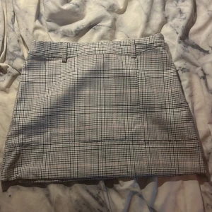 Rutig kjol från Reserved - Säljer en klassisk rutig kjol från Reserved i svart, grått och vitt. Kjolen har bälteshällor och rak passform, perfekt för en stilren look. Tyg i mjuk polyesterblandning. Längden är kort och passar till många olika outfits.