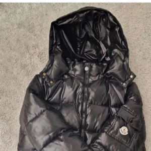 Moncler Maya - Säljer en svart dunjacka från Moncler med avtagbar huva och dragkedja framtill. Jackan har Moncler-logga på ärmen och praktiska fickor. Perfekt för kyliga dagar och riktigt snygg till streetwear. Ingen koll på hur mycket den kostar med det är en Moncler Maya som jag vill rensa bort från garderoben Mvh Elias