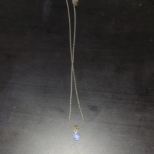 Silverfärgat halsband med blå sten - Ett stilrent halsband i silverfärg med en rund blå sten som hänge. Kedjan är tunn och enkel, vilket gör att den blå stenen verkligen står ut. Perfekt för dig som gillar diskreta men snygga smycken.