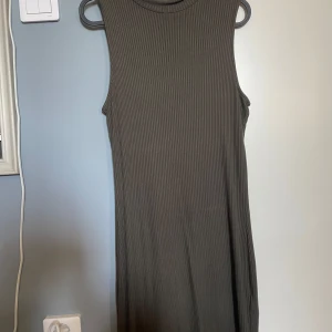 Ribbad ärmlös klänning från Gina Tricot - Säljer en ribbad, ärmlös klänning från Gina Tricot i en mörkgrön nyans. Klänningen har en rak passform och rund halsringning, perfekt för en stilren och enkel look. Materialet är mjukt och stretchigt för extra komfort.