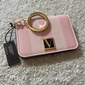 Rosa plånbok från Victoria's Secret - Säljer en söt rosa plånbok från Victoria's Secret med guldfärgad nyckelring och logga framtill. Plånboken har kortfack, fönster för ID och stängs med tryckknapp. Perfekt att ha med sig i väskan eller på nyckelknippan. Äkta och aldrig använd, lappen sitter kvar! 💕