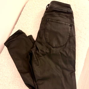 Svarta ”skinnbyxor” med dragkedja - Säljer ett par svarta skinnbyxor med dragkedja och fickor bak. Byxorna har en tight passform och ger en cool look till outfiten. Låga i midjan.  