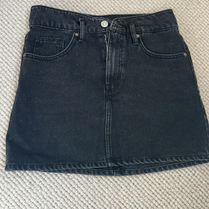 Svart jeanskjol från ZARA - Svart jeanskjol från ZARA med klassisk femficksdesign och dragkedja framtill. Kjolen har bälteshällor och raka sömmar, perfekt till vardagsstilen. Enkel och stilren modell som är lätt att matcha.