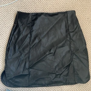 Svart kjol i skinnimitation från Zara - Säljer en svart kjol i skinnimitation från Zara. Kjolen har en enkel och stilren design med lätt A-linjeform och släta sömmar. Perfekt att styla med en stickad tröja eller en cool t-shirt.