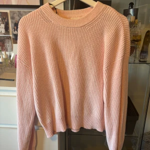 Ljusrosa stickad tröja från H&M - Säljer en ljusrosa stickad tröja från H&M. Tröjan har en klassisk rund halsringning och långa ärmar. Den är ribbstickad och har en avslappnad passform, perfekt för lager på lager under kyligare dagar. Dåligt ljus på bild, så tröjan förekommer mer gul på bild än i verklighet.