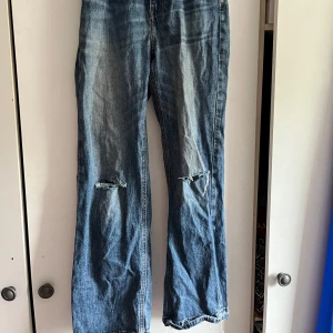 Blå jeans från Zara - Säljer ett par blå jeans från Zara med hål vid knäna. Jeansen har klassisk femficksdesign och hög midja. Perfekta för en avslappnad och trendig look. Är med åt baggy hållet. Storlek 34. Lämna prisförslag om priset inte passar 