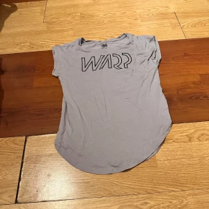 Ljusgrå t-shirt från  Stadium - Säljer en ljusgrå t-shirt från Stadium med tryck framtill. T-shirten har rund halsringning och korta ärmar. Perfekt för en avslappnad stil och enkel att matcha med jeans eller shorts.