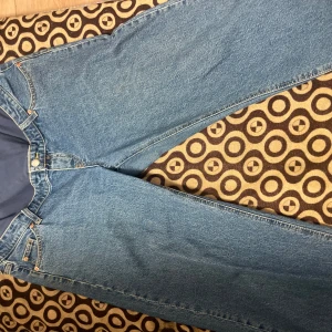 Blå mammabyxor i jeansmaterial - Säljer ett par blå mammabyxor i jeansmaterial med mjuk, stretchig mudd över magen. Klassisk femficksmodell med raka ben och normal passform. Perfekta för dig som vill ha bekväma jeans under graviditeten.
