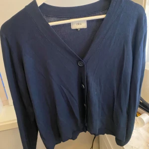 Mörkblå kofta från Ellos - Säljer en mörkblå kofta från Ellos i storlek XS. Koftan har v-ringning, två knappar framtill och långa ärmar. Perfekt att slänga över en topp för en enkel och stilren look. Lite stor i storlek så skulle nog säga S