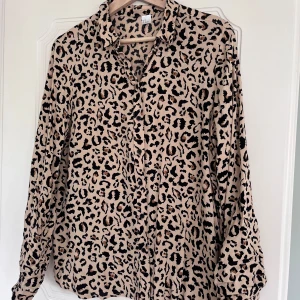 Beige leopardmönstrad skjorta - Säljer en beige skjorta med leopardmönster. Skjortan har klassisk krage, knäppning framtill och långa ärmar. Perfekt för dig som vill sticka ut med ett djurmönster i garderoben.