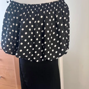 Set Svart offshoulder topp  med prickar och kjol - Säljer en svart offshoulder klänning med vita prickar. Klänningen har trekvartsärmar och en tight passform i midjan med dekorativa knappar. Perfekt för en stilren look!