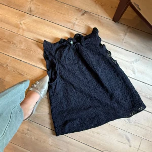 Svart blus med broderade blommor från & Other Stories - Säljer en svart blus från & Other Stories med vackert broderade blommor och volangdetaljer vid ärmslut och halsringning. Blusen är ärmlös och har en luftig, feminin känsla. Perfekt till sommaren!