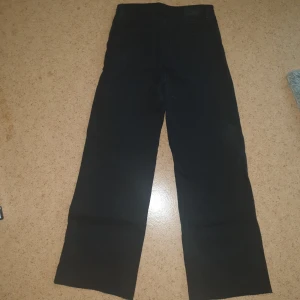 Svarta jeansbyxor från Monki - Svarta jeansbyxor från Monki med klassisk femficksdesign och raka ben. Byxorna har hög midja och stängs med dragkedja och knapp. Perfekta för en stilren och enkel look. De är i strl 26/34/xs.