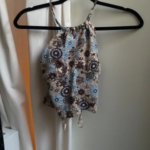 Blommig halterneck-linnetopp från Bik Bok - Säljer en söt halterneck-linnetopp från Bik Bok i beige med brunt och blått blommönster. Toppen har smala axelband som korsas i ryggen
