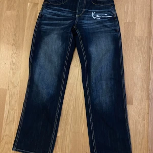 Mörkblå jeansbyxor från Karl Kani - Säljer ett par mörkblå jeansbyxor från Karl Kani med raka ben och kontrastsömmar. Byxorna har broderad logga fram och bak samt färgglada sömmar på bakfickorna. Perfekta för en streetwear-look.