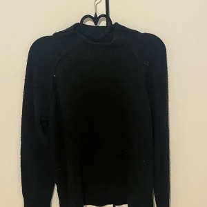 Svart stickad tröja från NA-KD - Säljer en svart stickad tröja från NA-KD i storlek XS. Tröjan har lång ärm och en hög ribbad halsringning som ger en snygg och stilren look. Perfekt att matcha med jeans eller kjol för en enkel och trendig outfit.