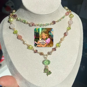 Färgglatt pärlhalsband med grön och rosa detalj - Unikt halsband med pärlor i grönt och rosa. Inspirerat av karaktären Flora från tv-serien Winx Club. Halsbandet har dubbla rader och en hänganande grön fjärilsberlock. Perfekt för dig som vill ha något färgglatt och lekfullt. 