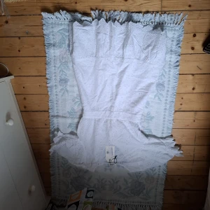 Vit kortklänning med volang och broderad detalj - Superfin vit kortklänning från Sisters Point med broderade detaljer och volangkant. Klänningen har v-ringning och korta ärmar, perfekt för sommarens alla tillfällen. Söt och feminin modell med markerad midja.