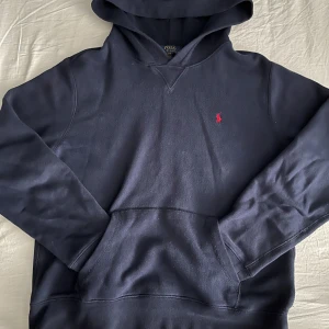 Mörkblå hoodie från Polo Ralph Lauren - Säljer en klassisk mörkblå hoodie från Polo Ralph Lauren med röd broderad logga på bröstet. Tröjan har huva och magficka, perfekt för en avslappnad stil. Passar dig som gillar tidlös design och hög kvalitet. Skriv gärna vid frågor eller förslag🙌