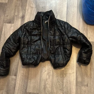 Svart croppad pufferjacka från Haan Fashion - Säljer en svart croppad pufferjacka från Haan Fashion. Jackan har hög krage, quiltad design och dragkedja som går hela vägen upp i ryggen. Perfekt för dig som vill ha en trendig och varm jacka med cool look.