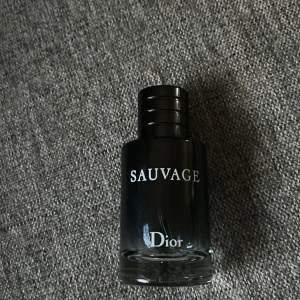 Sauvage Eau de Toilette från Dior - Säljer en Sauvage Eau de Toilette från Dior. Flaskan är svart med vit text och har en stilren, rund design. Korken är magnetisk och pryds av Diors logotyp. En klassisk herrdoft med modern känsla. Tar byten eller pengar 
