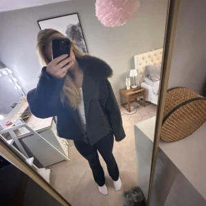 Svart kappa med fuskpäls från Meotine  - Säljer en svart kappa från Meotine med stor, fluffig päls runt kragen. Jackan bra passform och långa ärmar. Perfekt för kyliga dagar och ger en lyxig känsla till outfiten. Storleken är både S/M