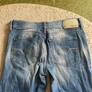 Blå utsvängda jeans från Diesel - Säljer ett par klassiska blå jeans från Diesel med utsvängda  ben och snygga slitningar. Byxorna har fem fickor, knappgylf och tydlig Diesel-logga på bakfickan. Passar dig som är runt 160cm.  Perfekta för en avslappnad stil. :)