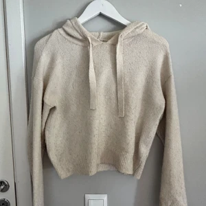 Beige stickad hoodie från JDY - Mysig beige stickad hoodie från JDY med huva och dragsko. Tröjan har en croppad passform och långa ärmar. Perfekt för lager-på-lager och chill dagar.