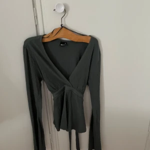 Grå omlottopp med knytband från Slanovskiy - Säljer en grå omlottopp från Slanovskiy med långa ärmar och knytband i midjan. Toppen har v-ringning och är tillverkad i ett mjukt, lätt strukturerat material. Perfekt för en stilren och trendig look.helt ny och nästan oanvänd 