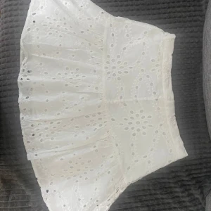 Vit broderad kjol från Amisu - Superfin vit kjol från Amisu med broderade detaljer och knappar framtill. Kjolen har ett luftigt tyg och ett vackert hålmönster som ger en romantisk känsla. Perfekt till varma dagar och enkel att matcha med olika toppar.