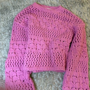 Ljuslila virkad stickad tröja - Superfin ljuslila stickad tröja med virkat mönster och lång ärm. Tröjan är croppad och har en luftig känsla, perfekt för lager på lager. Rund halsringning och mjukt material.