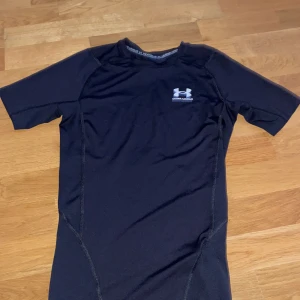 Svart kompressionströja från Under Armour - Säljer en svart kompressionst-shirt från Under Armour med korta ärmar och logga på bröstet. Perfekt för träning eller sport, tillverkad i syntetmaterial som andas och håller dig torr. Sitter tight mot kroppen för maximal rörelsefrihet. Inga defekter.