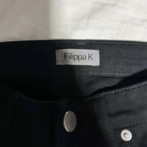 Svarta jeans från Filippa K - Snygga svarta jeans från Filippa K med klassisk design och knappstängning. Byxorna har fem fickor och är tillverkade i ett bekvämt material som passar perfekt för en stilren look.