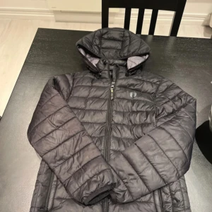 Svart pufferjacka med huva - Säljer en svart pufferjacka med huva och dragkedja framtill. Jackan har lång ärm och quiltad design som ger en sportig look. Perfekt för kyligare dagar och enkel att matcha med olika outfits.