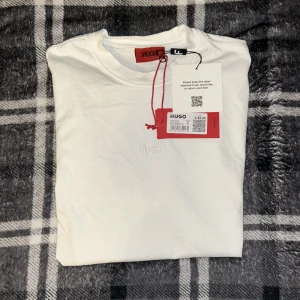 Vit t-shirt från HUGO - Säljer en stilren vit t-shirt från HUGO med diskret broderad logga på bröstet. Klassisk passform och rund halsringning. Perfekt basplagg för garderoben.