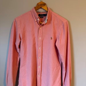Ralph lauren skjorta - Rosa Ralph Lauren skjorta med blå ränder i kragen och inuti ärmarna, nypris ca 1500, använd väldigt få gånger och inga defekter, perfekt för sommaren