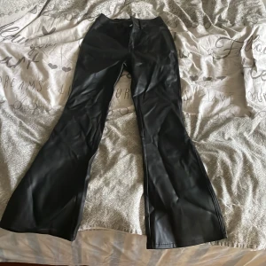 Svarta bootcut byxor i skinnimitation - Säljer ett par svarta bootcut byxor i skinnimitation. Byxorna har mellan midja och en snygg glansig finish som ger en cool look. Perfekta för dig som vill sticka ut med en trendig stil. Byxorna är perfekta för en ute kväll med tjejerna.