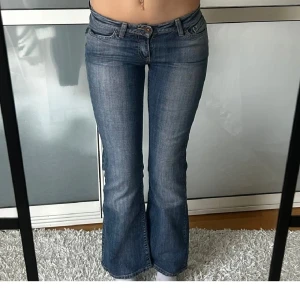 Blå bootcut jeans - Snygga blå bootcut jeans med låg midja och klassisk femficksdesign. Jeansen har en lätt tvättad look och sitter tight upptill med utsvängda ben. Perfekta för en avslappnad stil. 