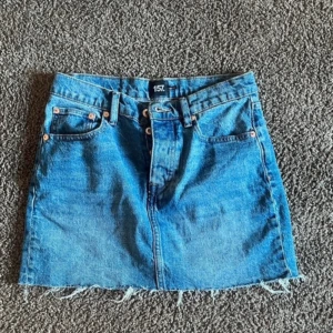 Blå jeanskjol från 157 - Säljer en klassisk blå jeanskjol från 157, modell Maddy. Kjolen har fem fickor, bälteshällor och rå kant nertill för en trendig look. Perfekt till vardags och enkel att matcha med olika toppar.