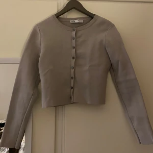 Ljusgrå croppad kofta från Zara - Säljer en ljusgrå croppad kofta från Zara med rund halsringning och knappar framtill. Tröjan är stickad och har långa ärmar. Bra och robust material🌸