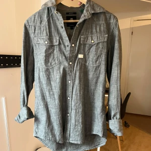 Grå skjorta  - Säljer en grå skjorta från G-Star RAW i slim fit-modell. Skjortan har långa ärmar, två bröstfickor med knappar och klassisk krage. 