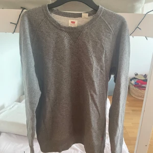 Grå sweatshirt från Levi's - Säljer en klassisk grå sweatshirt från Levi's i storlek L. Tröjan har rund halsringning och långa ärmar. Perfekt basic-plagg med enkel design och mjukt material.